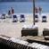 Guests relaxing on a sandy shoreline with beach chairs and a shaded seating area